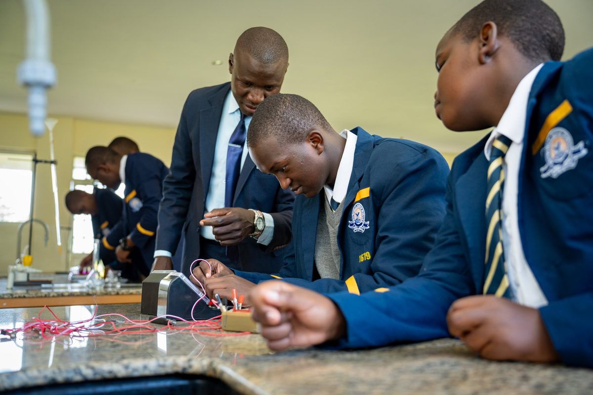 A teacher helps two boys with a circuit
