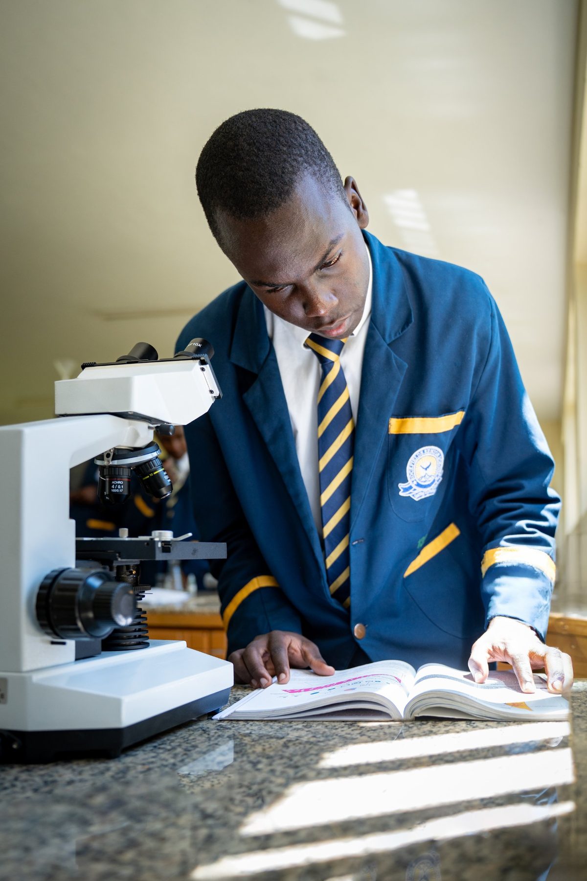 A boy checks his textbook beside a microscope